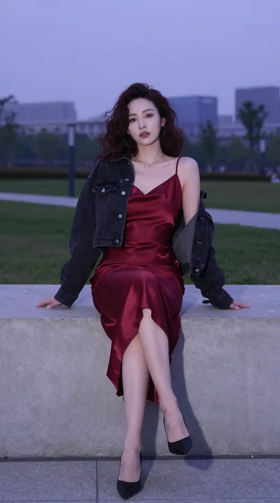 Woman in red satin dress above urban park at dusk