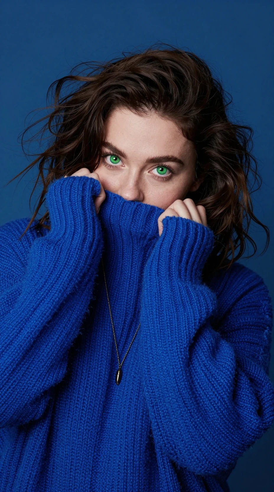 Playful woman hiding in oversized blue knitted sweater