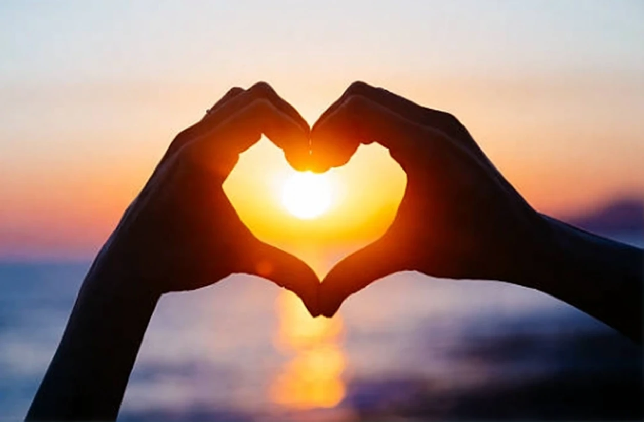 Hands forming a heart shape around a glowing sunset sun