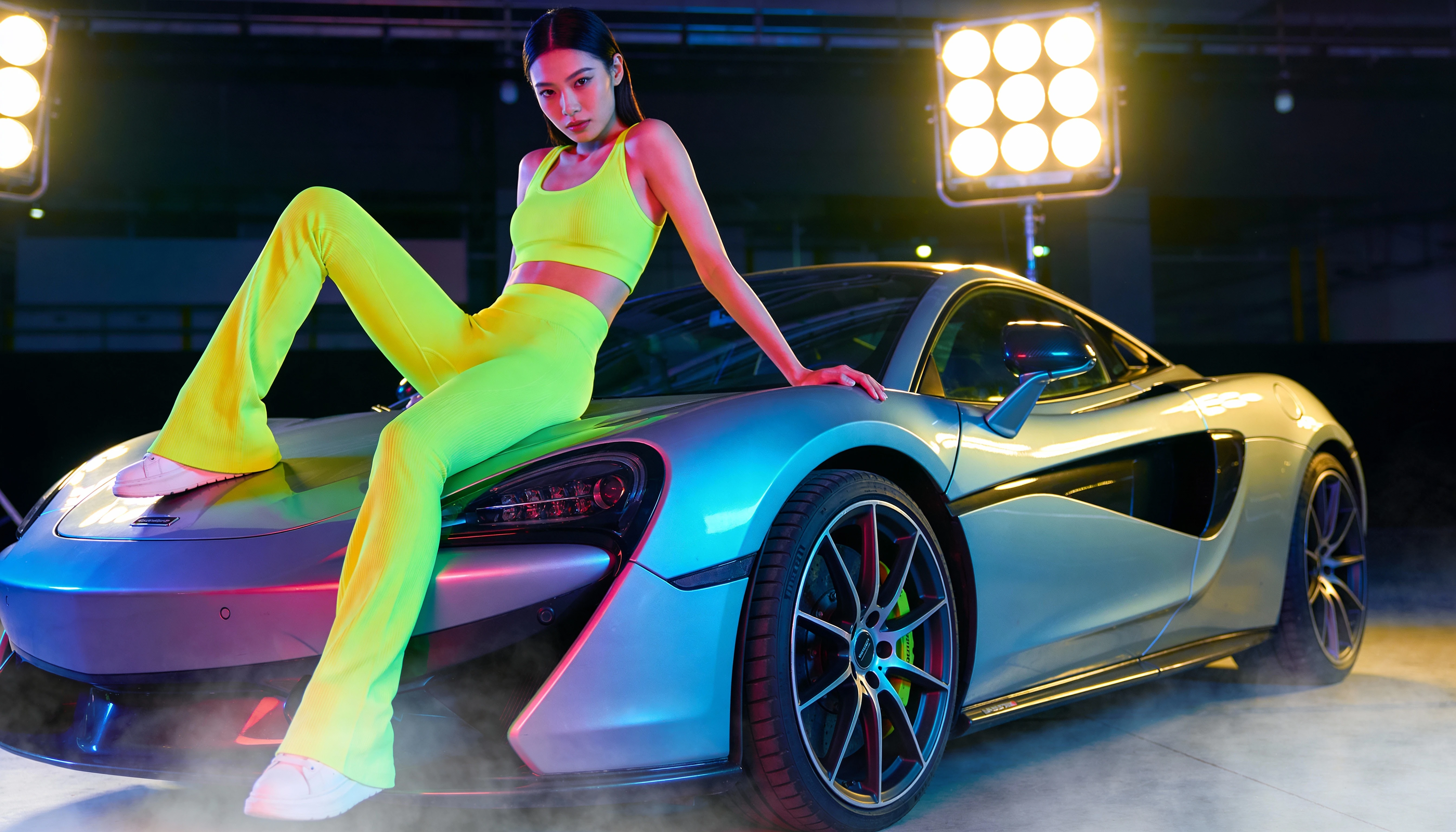 Asian woman in neon sportswear on sports car in studio