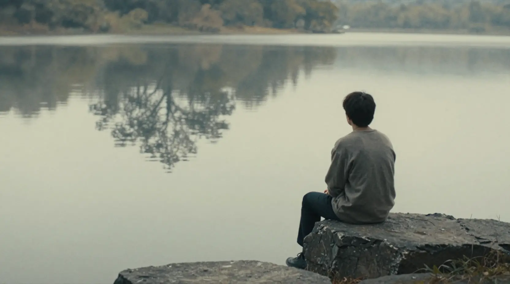 Lone figure on stone by tranquil reflective lake