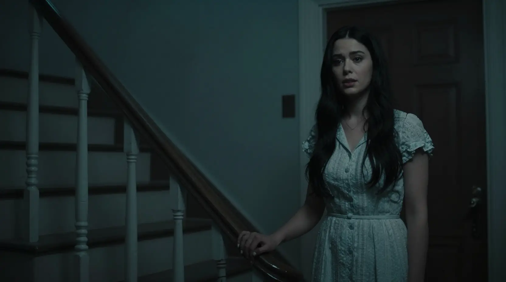 Woman by her door in a dark cinematic stairwell
