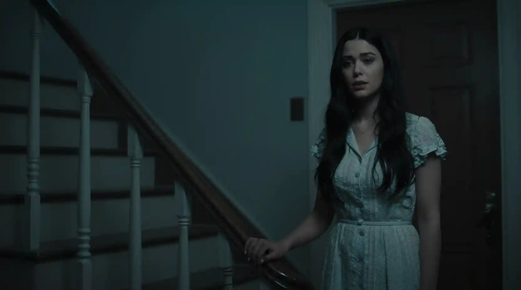 Woman by her door in a dark cinematic stairwell
