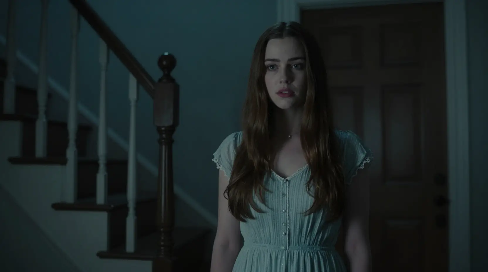 Young woman at her front door in a dim stairwell