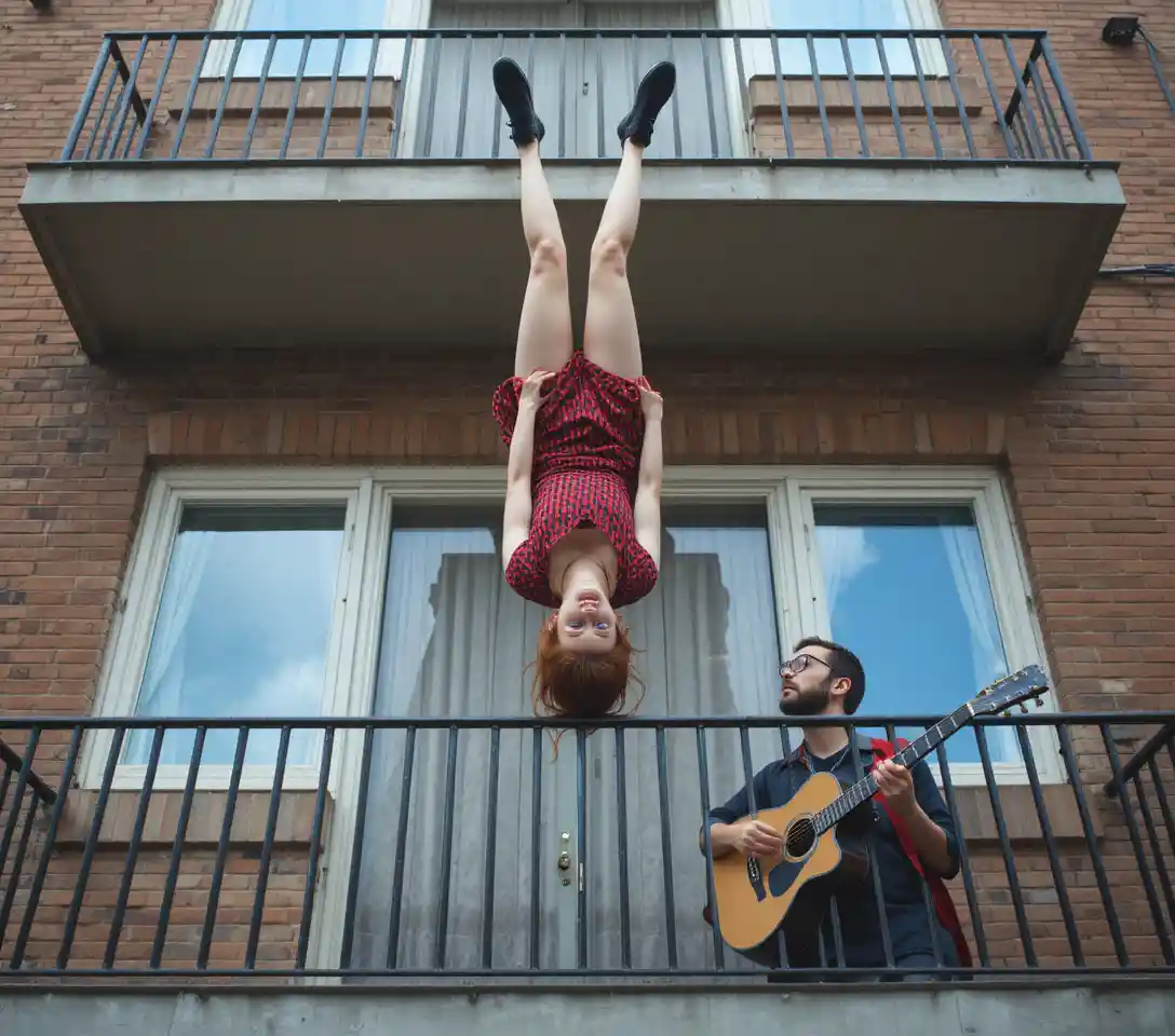 Woman doing a balcony handstand above guitarist on street
