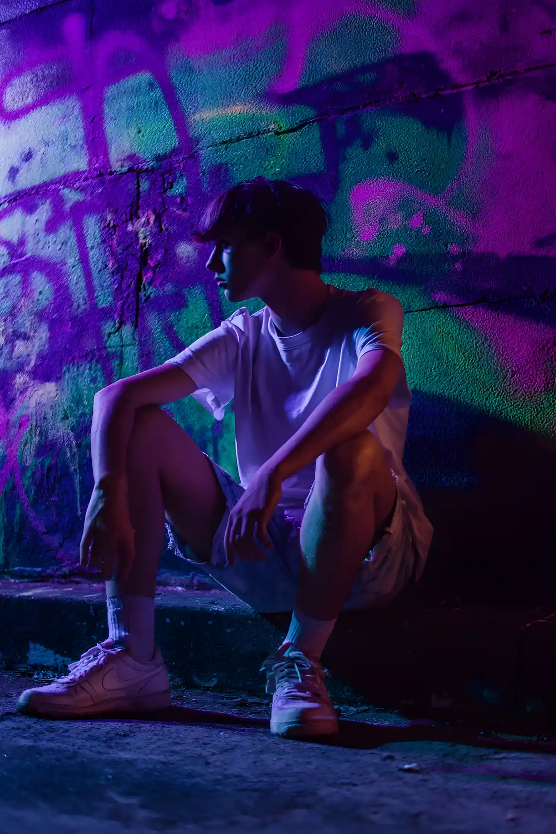 Young man sitting by neon graffiti wall at night