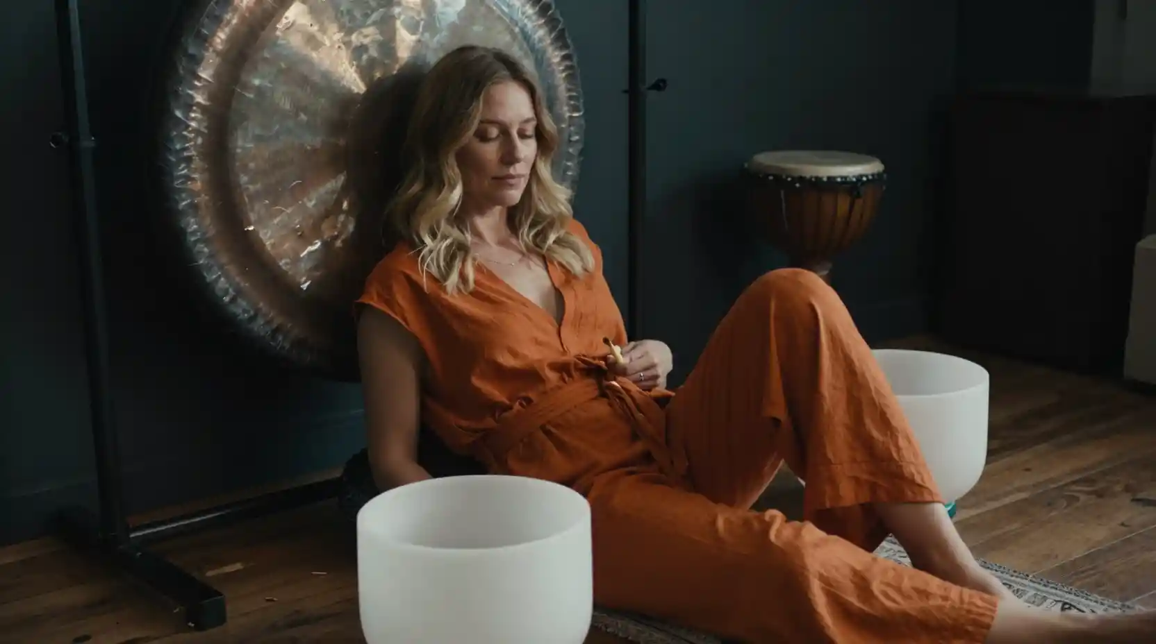 Blonde woman in orange jumpsuit playing a white sound bowl