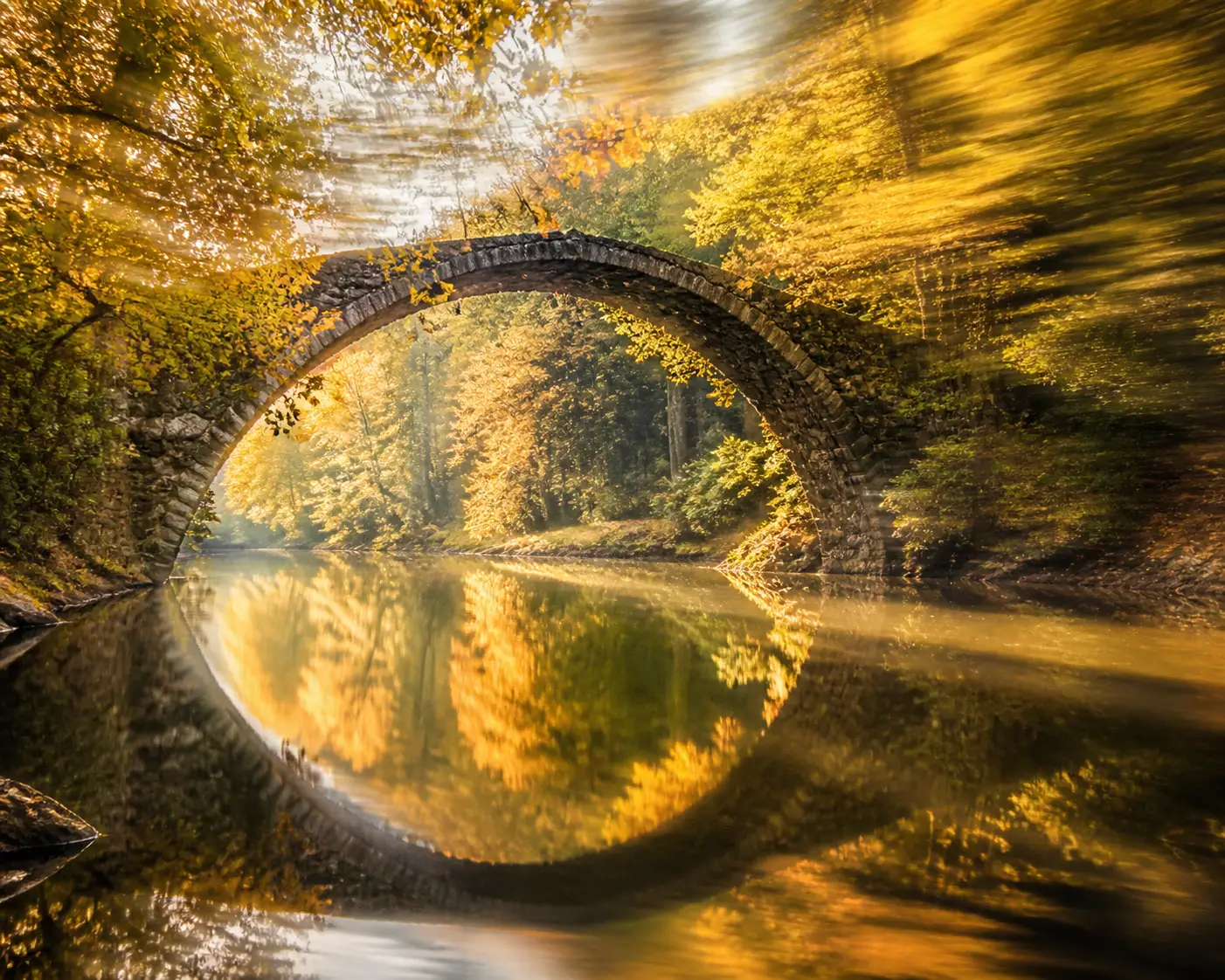 Ancien pont de pierre se reflétant sur une rivière calme d’automne