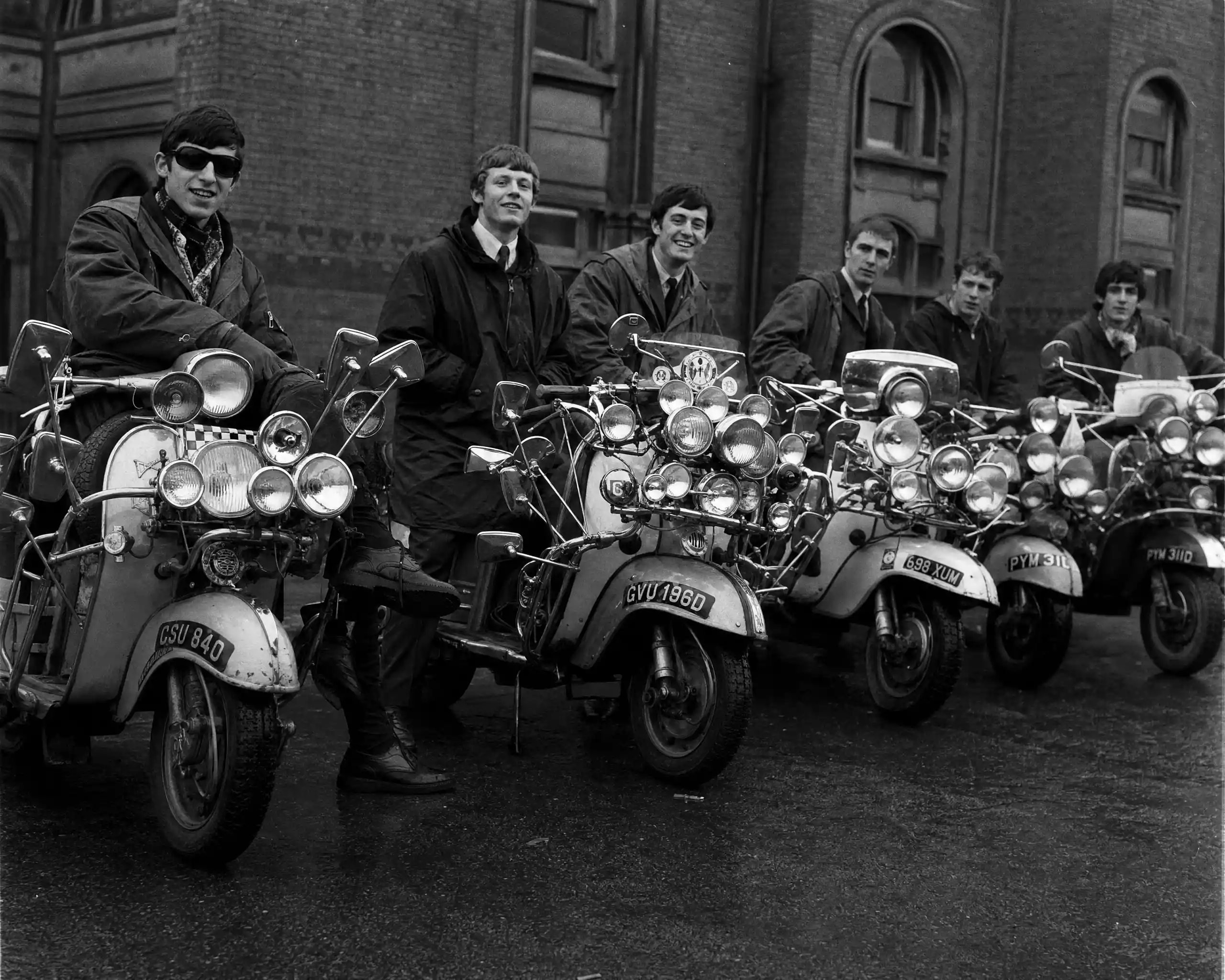 Young men with vintage scooters outside brick building