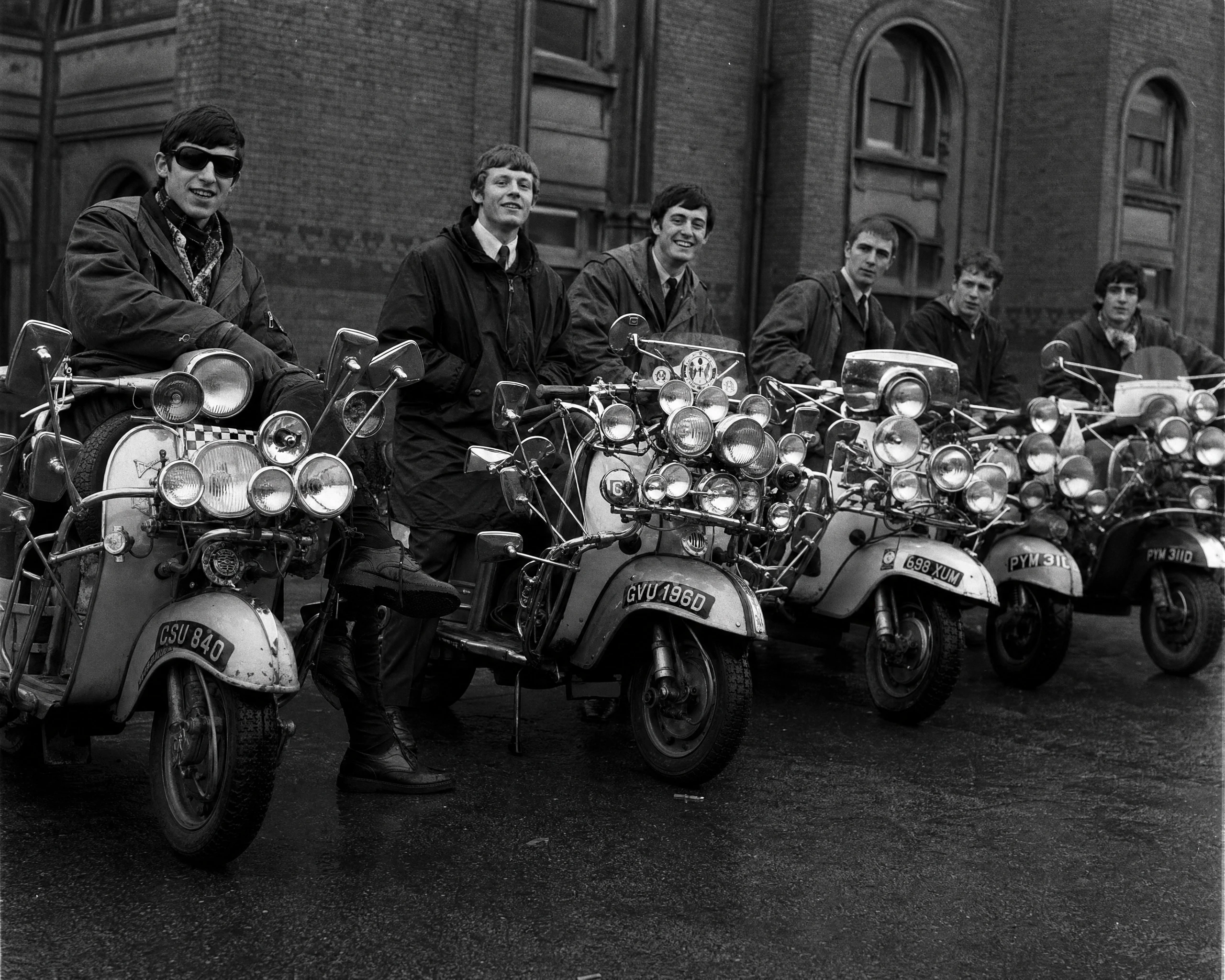 Young men with vintage scooters outside brick building