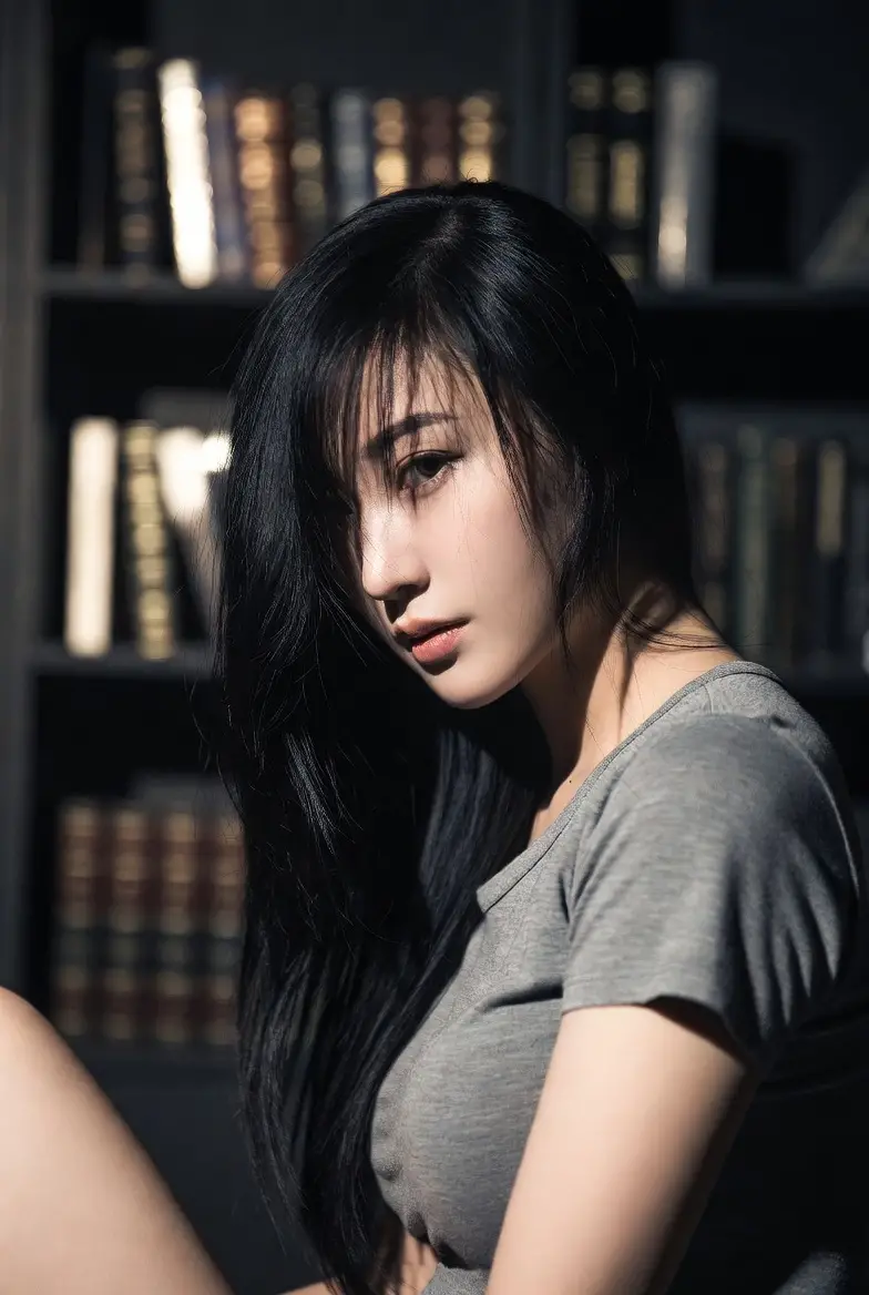 Asian woman sitting on floor by bookshelf in soft light