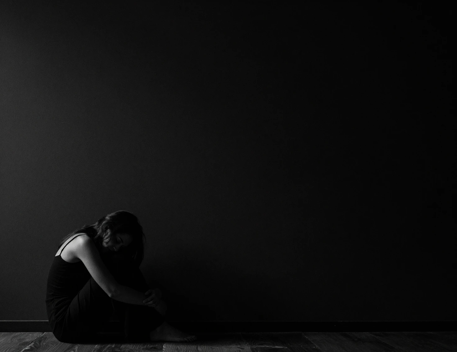 Woman curled up in darkness against a vast empty wall