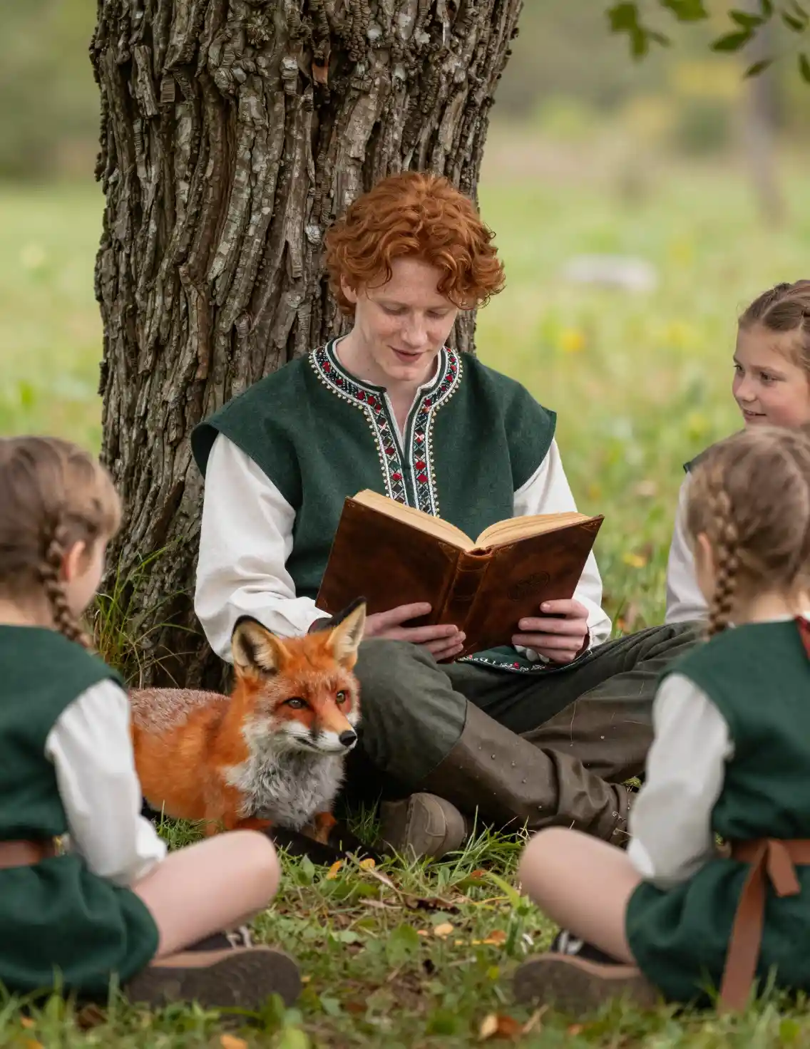 Young man reading under a forest tree with a fox nearby