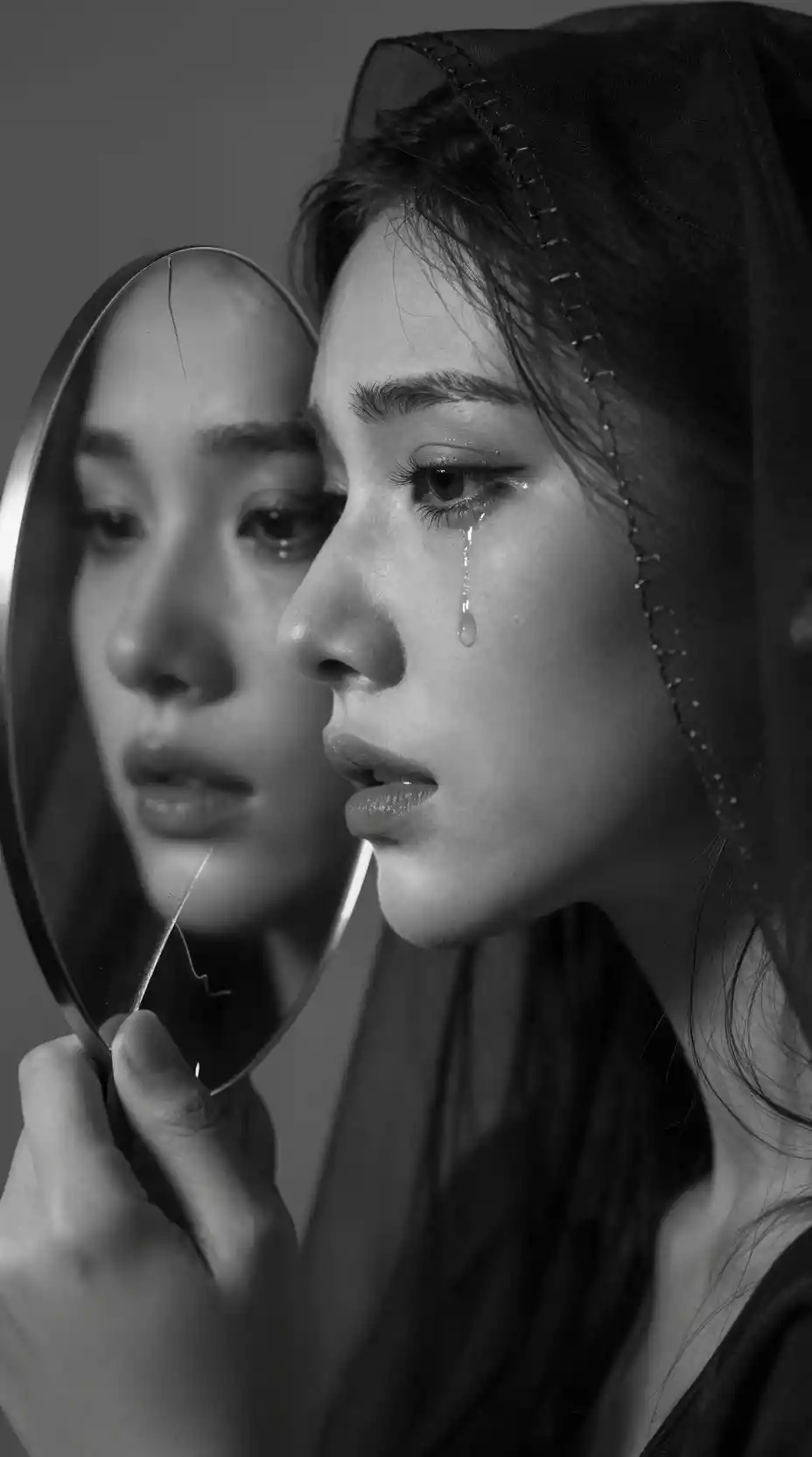 Grayscale close up of a veiled girl with a fractured mirror