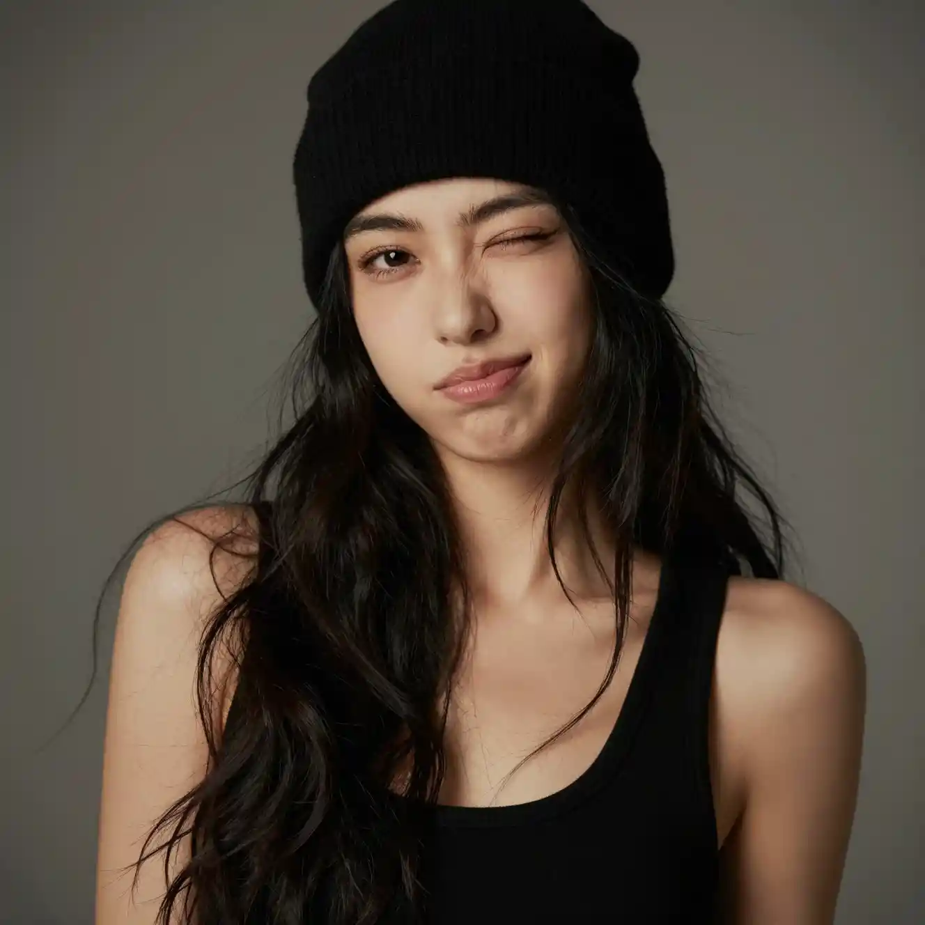 Playful young woman in beanie and black tank top portrait