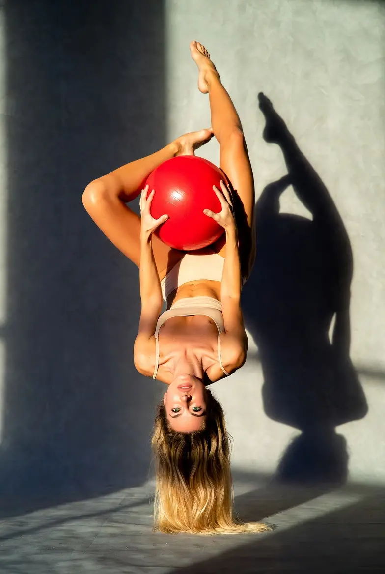 Mulher em postura de ioga equilibrando bola vermelha no estúdio