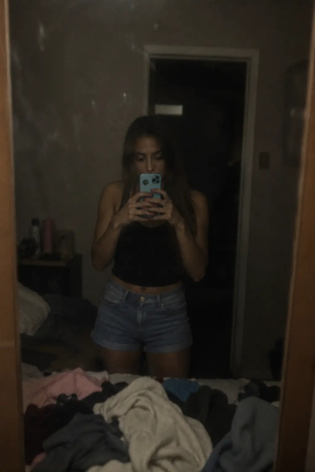 Mujer tomándose una selfie en el espejo en un dormitorio desordenado