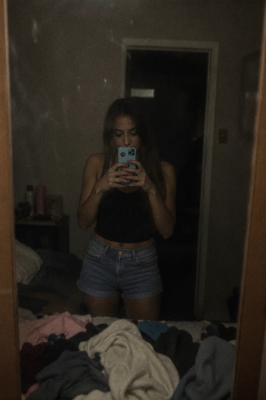 Mujer tomándose una selfie en el espejo en un dormitorio desordenado