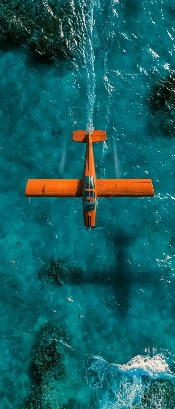 ターコイズブルーの海の上を飛ぶヴィンテージオレンジの飛行機