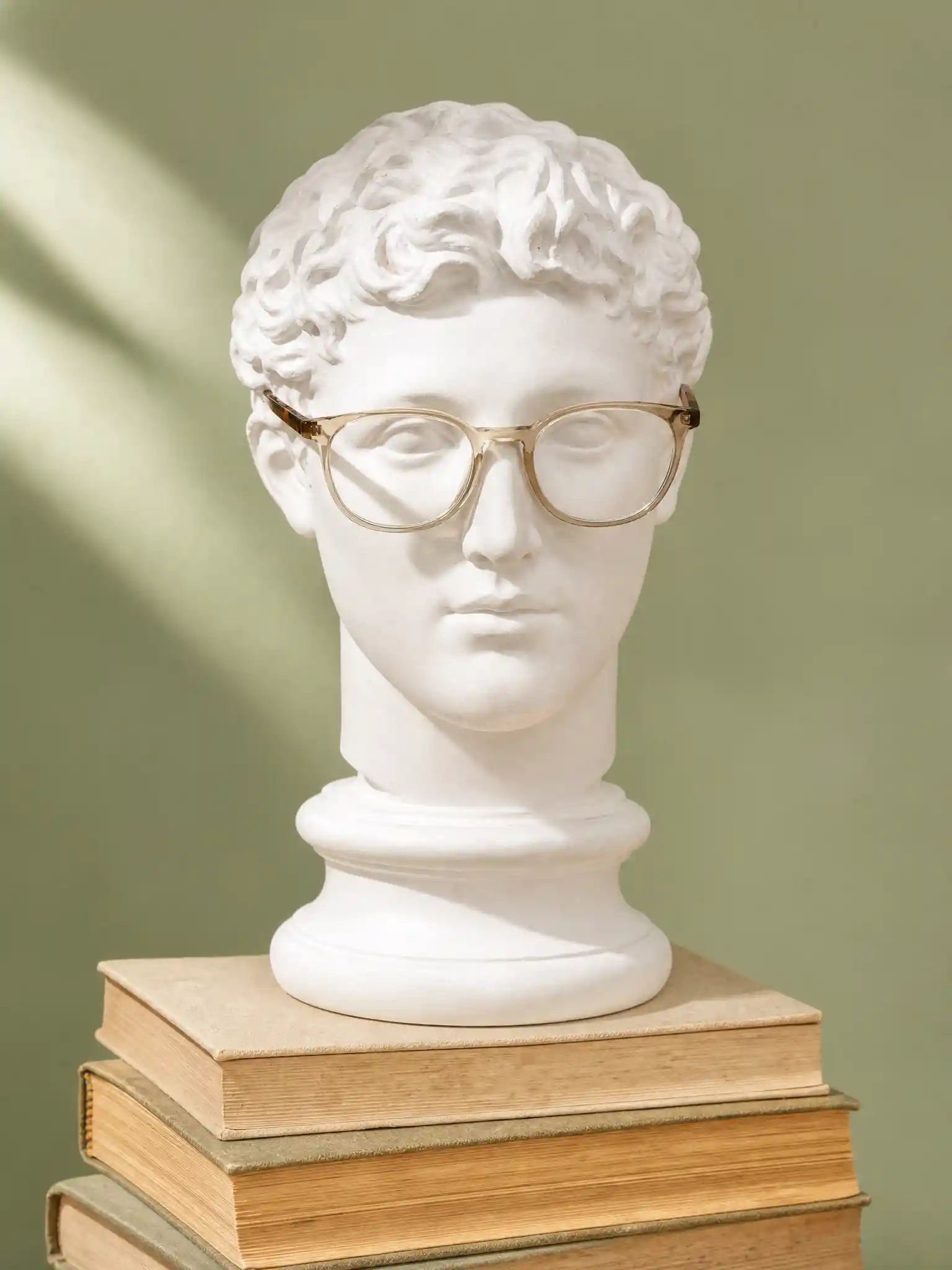 Busto clásico con gafas de diseñador sobre libros vintage