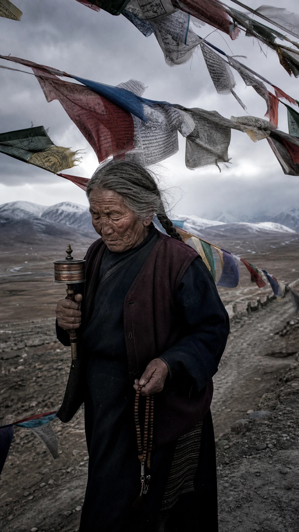 Elderly Tibetan woman walking under weathered prayer flags