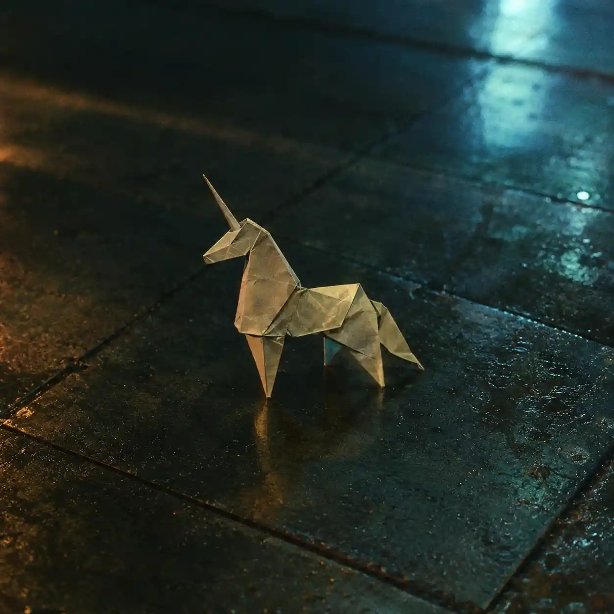 Paper origami unicorn on a dark wet tiled floor