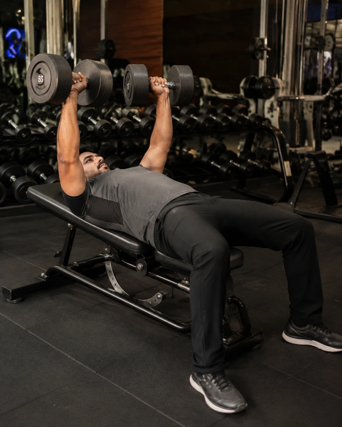 Indian man doing dumbbell bench press in a modern gym