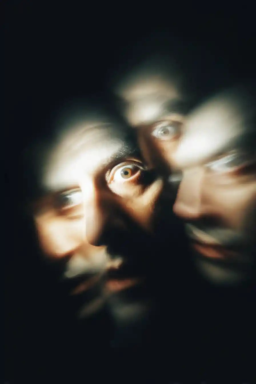 Blurred face fading into darkness with unblinking eyes