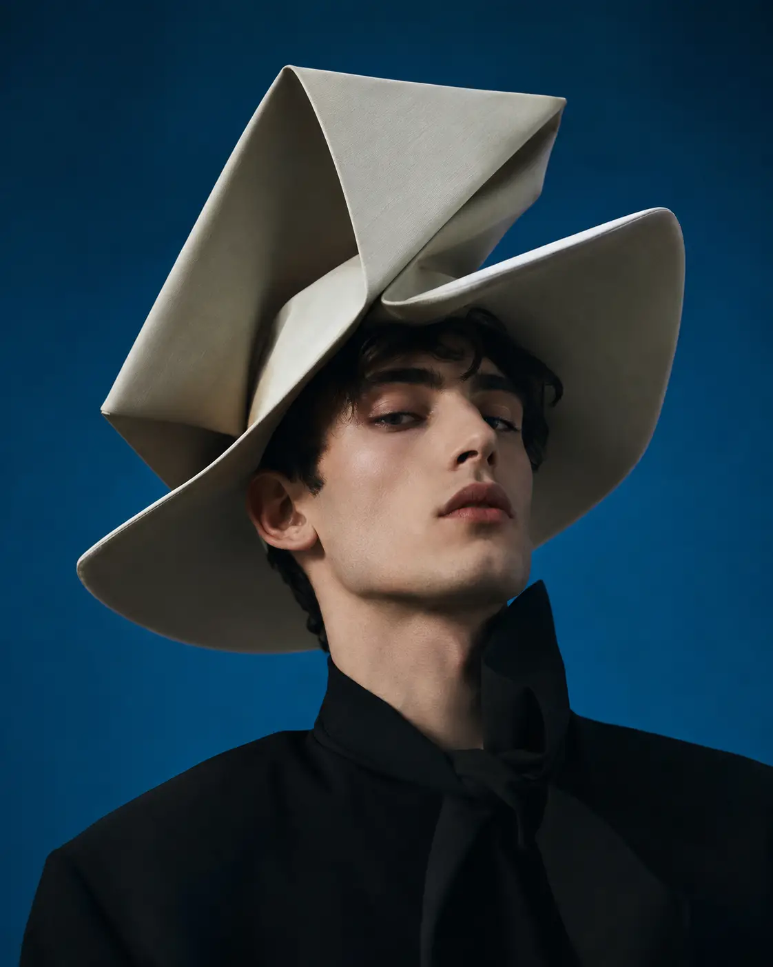 Homme avec chapeau avant-gardiste sur fond de studio bleu épuré