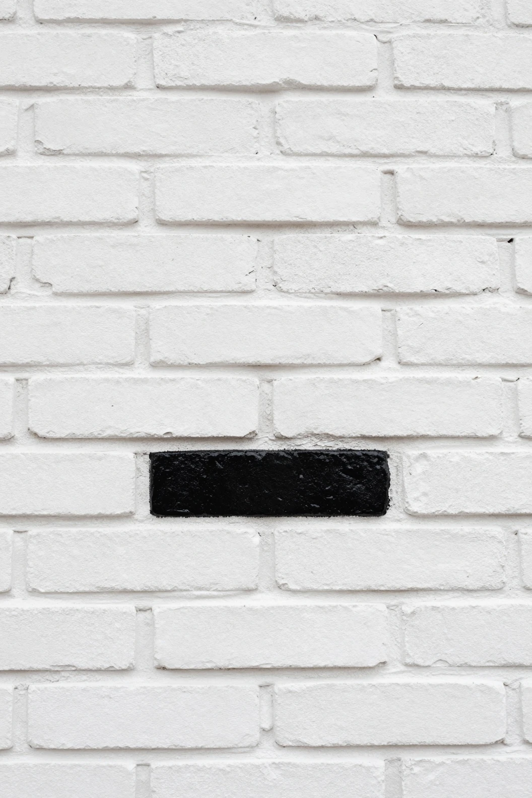 White brick wall with a single glossy black brick center