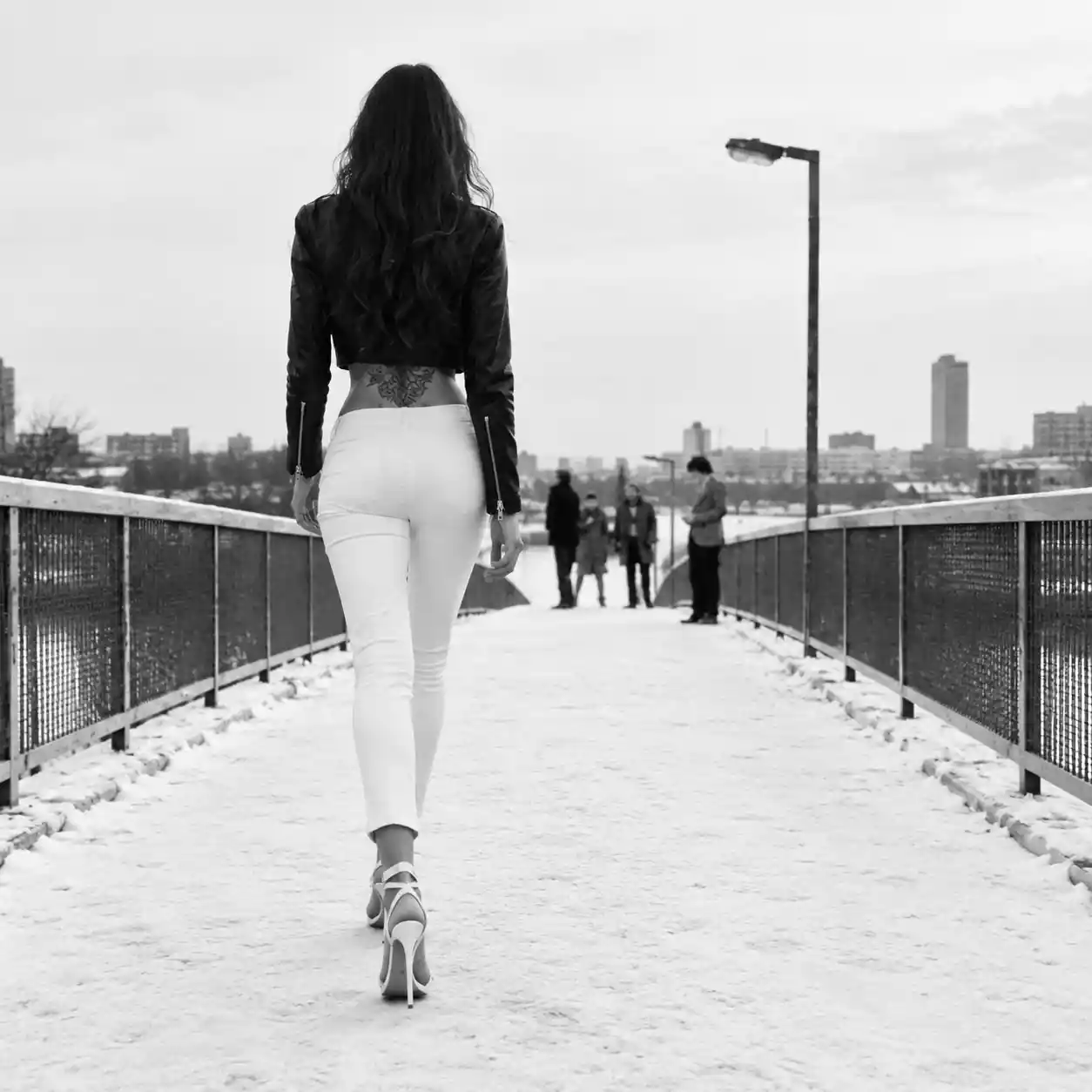 Joven caminando con tacones por un puente peatonal urbano