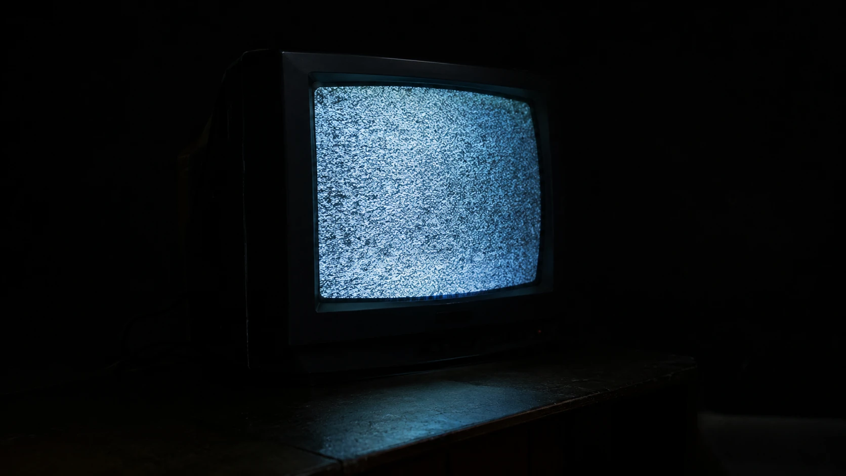 An old CRT television glows with static in a pitch-dark room