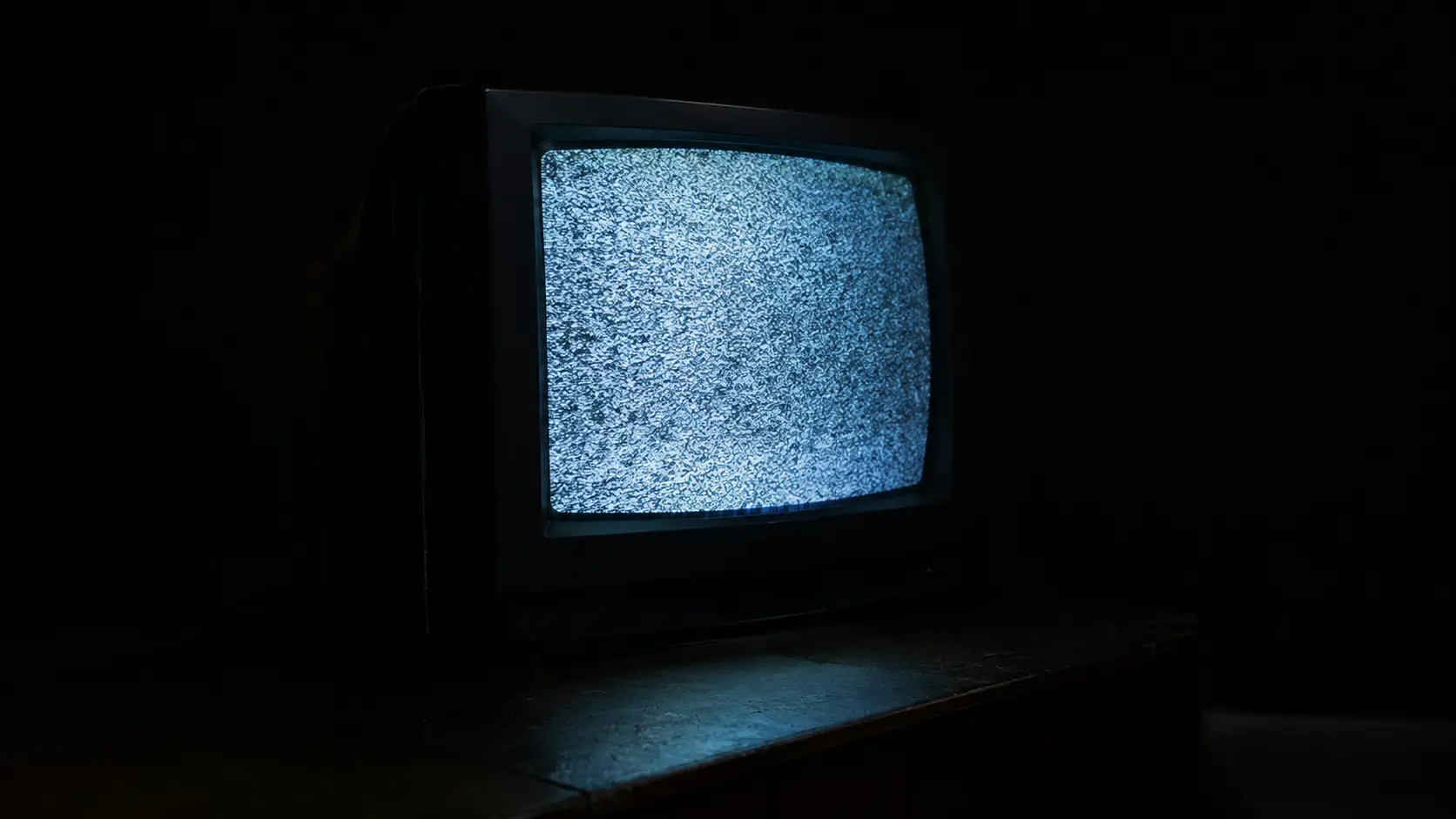 An old CRT television glows with static in a pitch-dark room