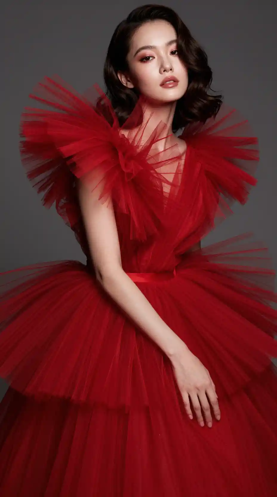 A poised woman in a voluminous scarlet tulle gown