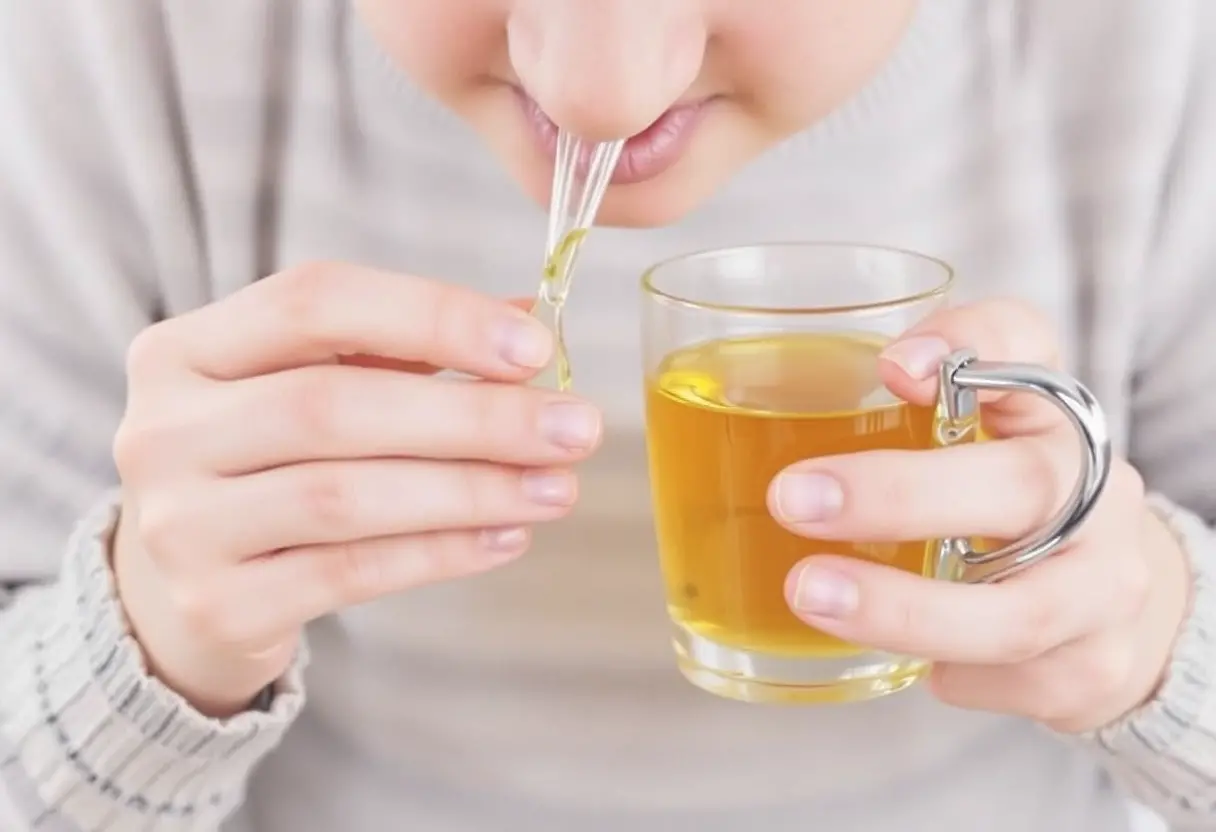 A person using a nasal inhaler while holding a glass mug of tea with a carabiner handle.