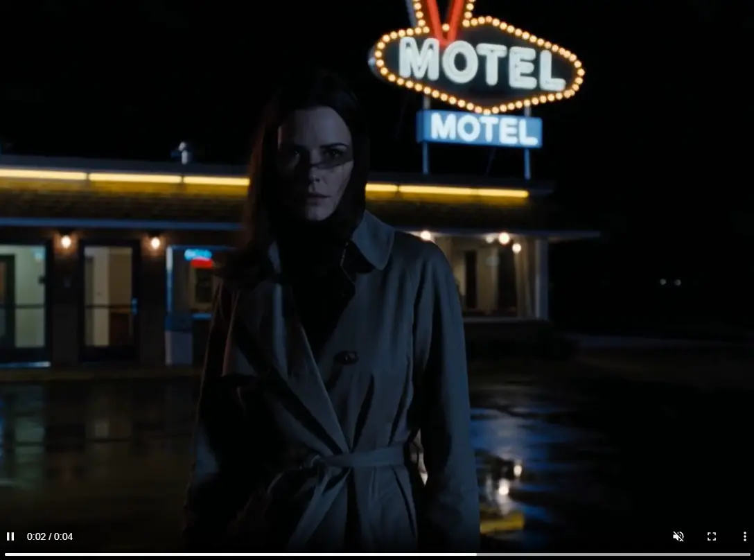 a woman slowly turns toward the camera while the motel sign flickers behind her