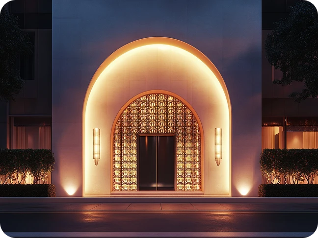 Una fachada de edificio moderno con un arco de entrada iluminado y vidrio con patrones geométricos.